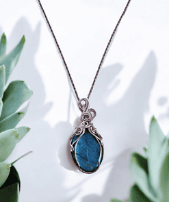 Bohemian wire-wrapped pendant with blue healing crystal and vintage-style wire, surrounded by green succulent leaves.