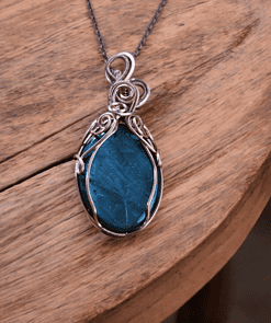 Wire wrapped gemstone pendant with custom silver wire design, handcrafted and resting on a wooden surface.