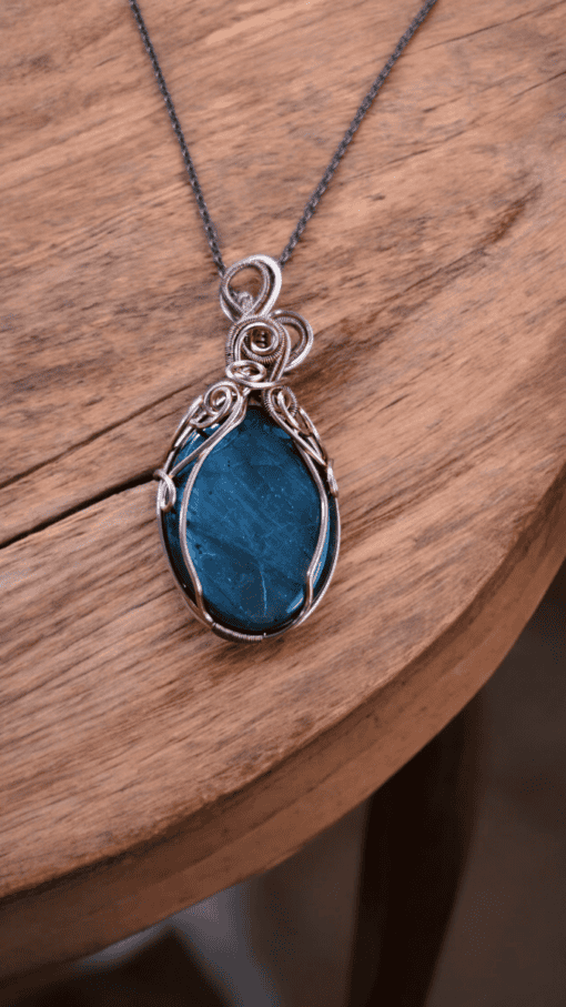 Wire wrapped gemstone pendant with custom silver wire design, handcrafted and resting on a wooden surface.