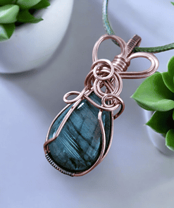 Nature-inspired luxury wire wrap pendant with green stone, intricately crafted, displayed beside succulent plants.