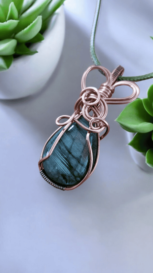 Nature-inspired luxury wire wrap pendant with green stone, intricately crafted, displayed beside succulent plants.