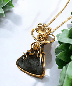 Gold wire-wrapped black stone pendant necklace on a white background, surrounded by green succulent plants.