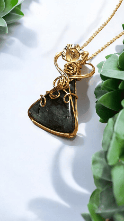 Gold wire-wrapped black stone pendant necklace on a white background, surrounded by green succulent plants.