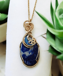 Gold wire-wrapped blue stone pendant with crescent moon and star design, displayed with green succulent plants.