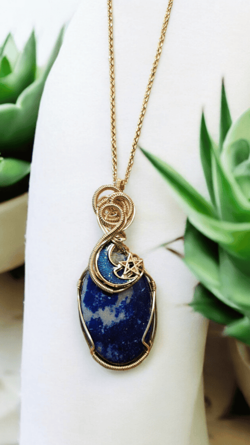 Gold wire-wrapped blue stone pendant with crescent moon and star design, displayed with green succulent plants.