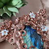 Copper wire pendant with a blue-green gemstone, decorated with light blue and copper flowers, next to a small green succulent.