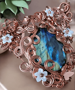 Copper wire pendant with a blue-green gemstone, decorated with light blue and copper flowers, next to a small green succulent.