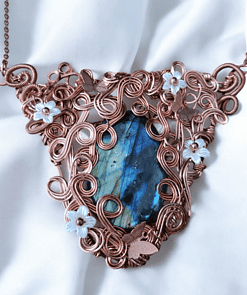 Copper wire necklace with blue gemstone, intricate swirls, butterflies, and flower designs, displayed on white fabric.