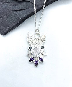 Silver pendant necklace with intricate detailing, featuring a central square gemstone and surrounded by small purple gems.