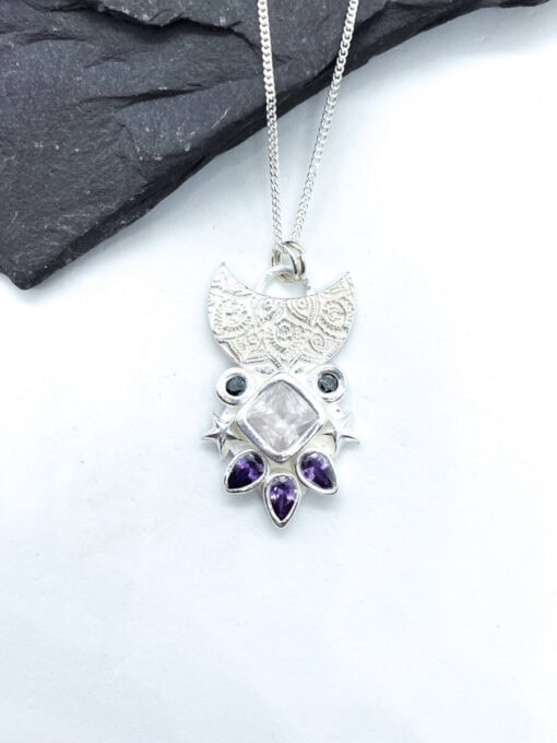 Silver pendant necklace with intricate detailing, featuring a central square gemstone and surrounded by small purple gems.