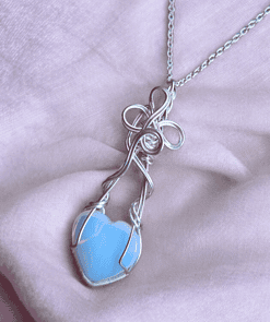 Handcrafted heart jewellery featuring a delicate blue heart charm necklace with intricate wire wrapping, on a soft pink background.