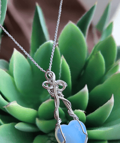 Artisan heart-shaped blue pendant necklace with intricate silver wire wrapped design, displayed atop a green succulent.