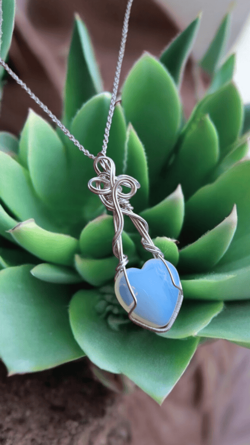 Artisan heart-shaped blue pendant necklace with intricate silver wire wrapped design, displayed atop a green succulent.