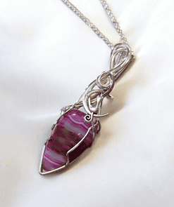 Silver wire-wrapped purple gemstone pendant necklace on white fabric background.