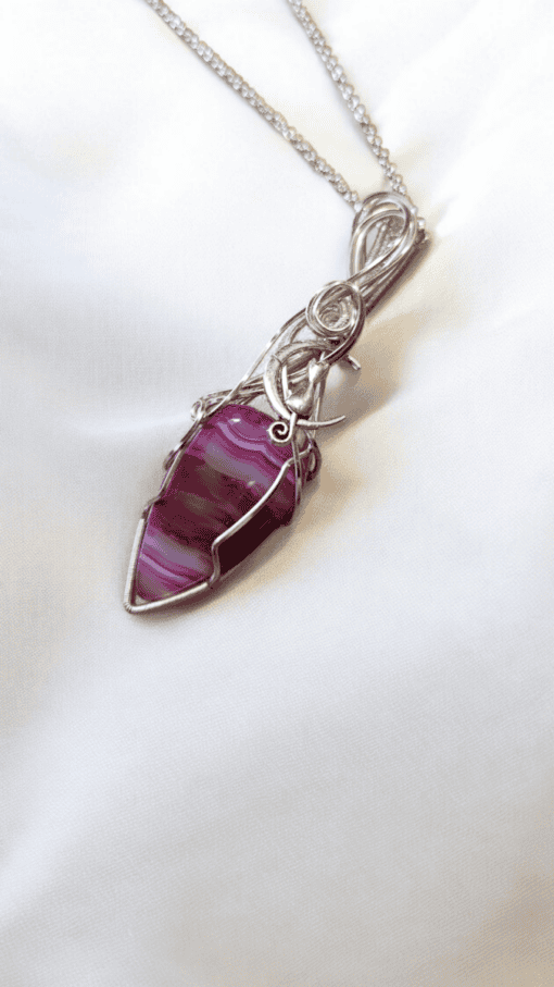 Silver wire-wrapped purple gemstone pendant necklace on white fabric background.