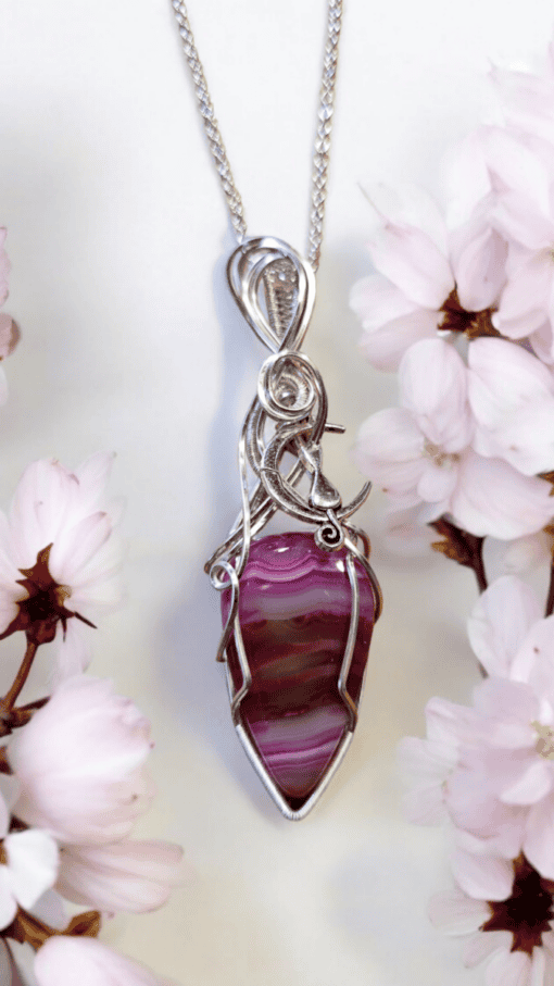 Silver chain necklace with intricate wire wrap design, featuring a pink and purple striped stone pendant, surrounded by cherry blossoms.