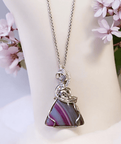 Silver wire-wrapped necklace with a triangular purple and grey pendant, displayed on a white bust with pink flowers.