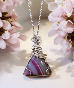 Silver pendant with a pink and purple striped stone, surrounded by delicate pink flowers on a light background.