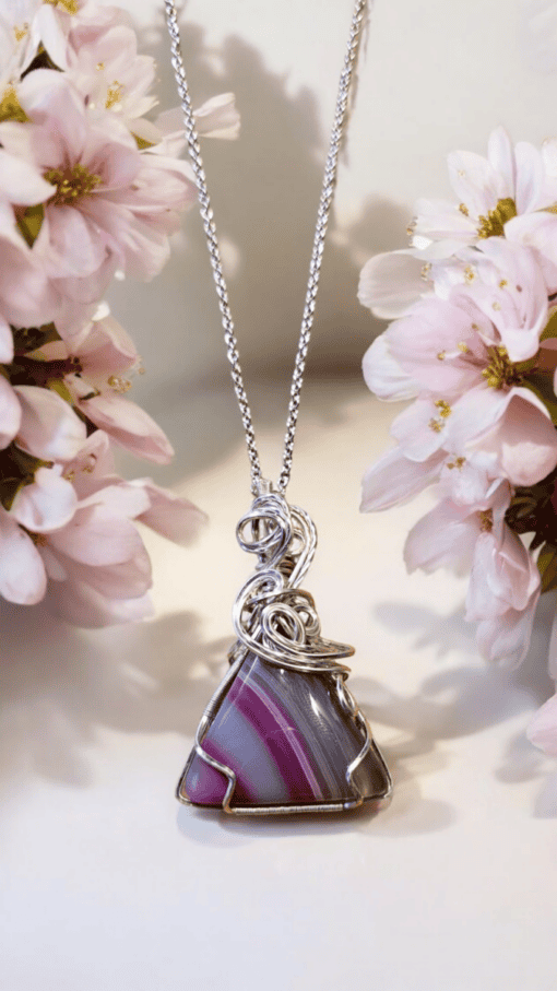 Silver pendant with a pink and purple striped stone, surrounded by delicate pink flowers on a light background.