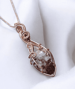 Intricately designed pendant with a stone wrapped in copper wire, on a white fabric background.