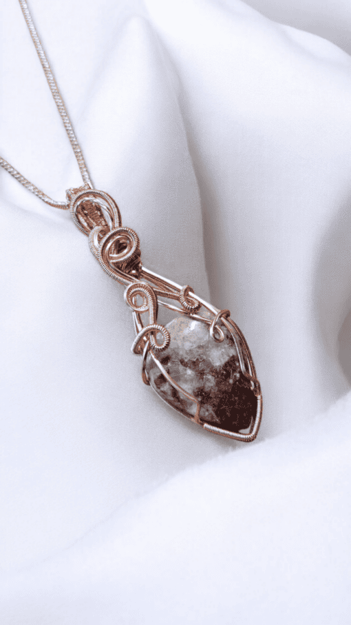 Intricately designed pendant with a stone wrapped in copper wire, on a white fabric background.