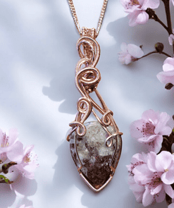 Rose gold wire-wrapped pendant with a stone, displayed among pink cherry blossoms against a light background.