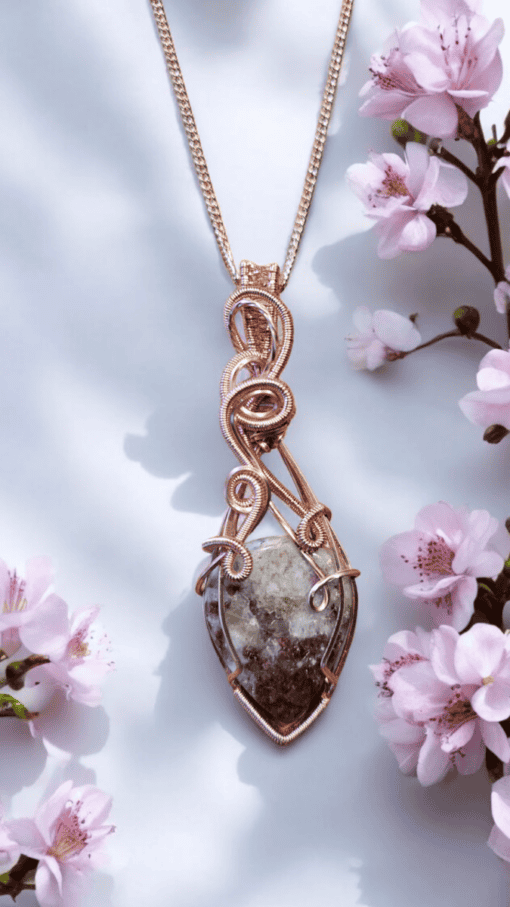 Rose gold wire-wrapped pendant with a stone, displayed among pink cherry blossoms against a light background.