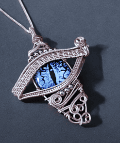 Intricate silver wire-wrapped pendant with a blue cat-eye stone at the center, resembling an eye, on a dark background.