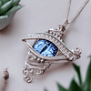 Intricate silver wire-wrapped pendant with a blue eye design, placed among green succulents on a light background.