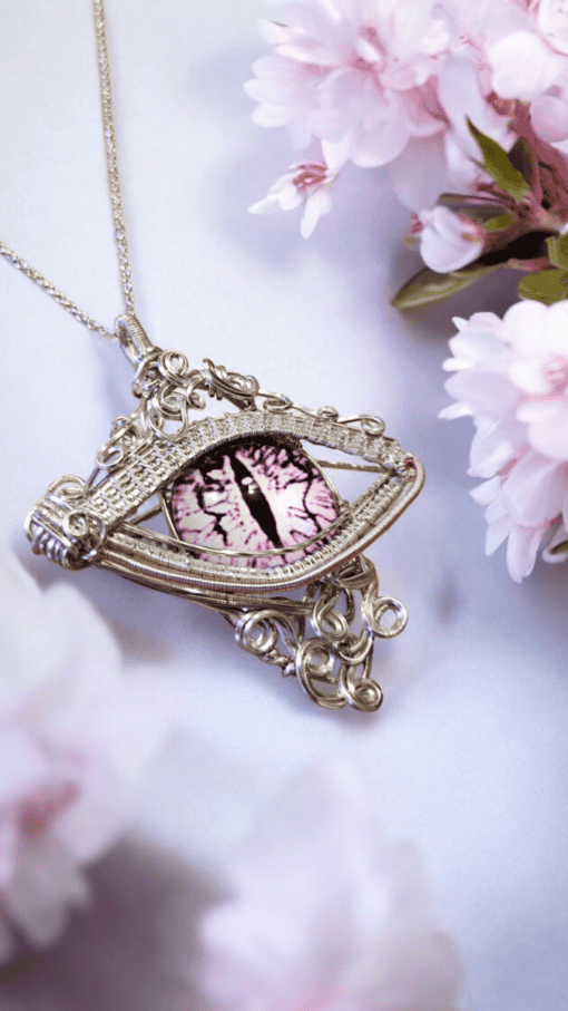 Ornate silver necklace featuring a decorative eye-like pendant with a purple iris, surrounded by pink flowers.