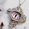 Intricately designed pendant resembling an eye with a purple iris, surrounded by delicate, blooming pink flowers.