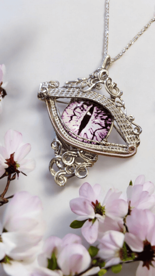 Intricately designed pendant resembling an eye with a purple iris, surrounded by delicate, blooming pink flowers.