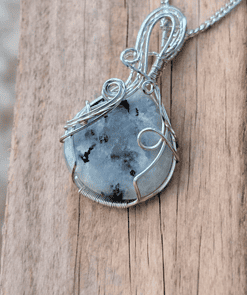 Silver wire-wrapped pendant with a large white and black speckled gemstone, placed on a wooden surface.