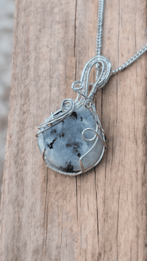 Silver wire-wrapped pendant with a large white and black speckled gemstone, placed on a wooden surface.