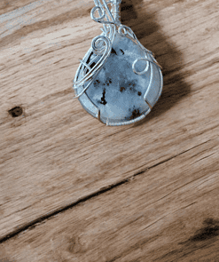 Silver wire-wrapped pendant with a translucent stone featuring black inclusions, displayed on a wooden surface.