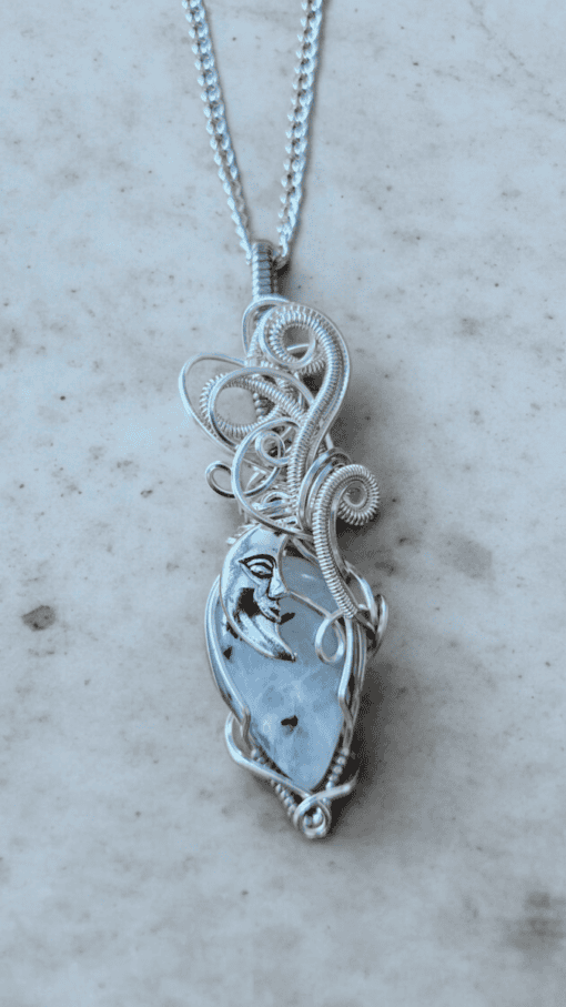 Intricate silver wire-wrapped pendant featuring a crescent moon face design, hanging on a silver chain.