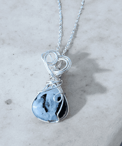 A silver wire-wrapped pendant with a blue and black marbled stone, displayed on a light gray marble surface.