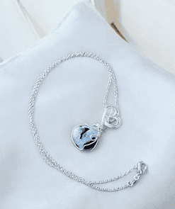 Silver necklace with a blue and black heart-shaped stone pendant, displayed on a light gray fabric background.