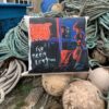 A pillow with graffiti art design on ropes and fishing buoys, background of stone building and blue bins.