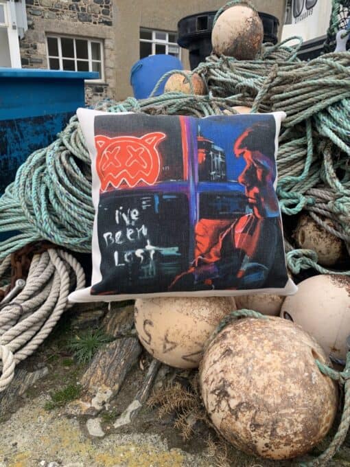 A pillow with graffiti art design on ropes and fishing buoys, background of stone building and blue bins.