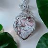 A silver wire-wrapped pendant featuring a marbled stone with intricate patterns, set against a backdrop of green leaves.