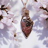 Gold pendant necklace with a teardrop-shaped stone, surrounded by blooming white flowers on either side.