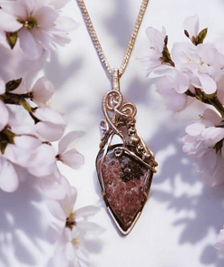 Gold pendant necklace with a teardrop-shaped stone, surrounded by blooming white flowers on either side.