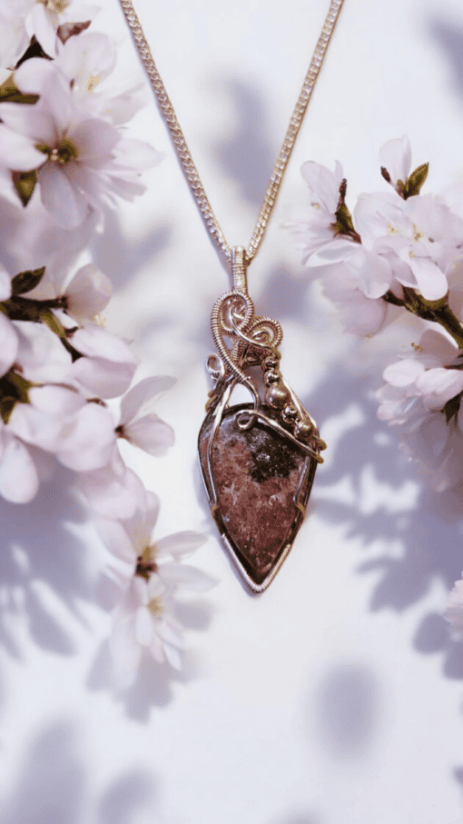 Gold pendant necklace with a teardrop-shaped stone, surrounded by blooming white flowers on either side.