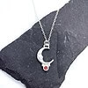 Silver necklace with moon pendant and red gemstone, displayed on a black slate background.