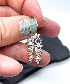 Hand holding star-shaped silver earrings with amber gemstones against a blurred background.