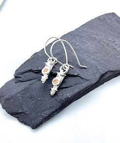 Silver star and scroll earrings with small orange gemstones, displayed on a dark slate platform against a light background.