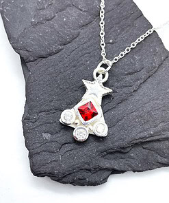 Silver necklace with a star and three gems, featuring a red central gem, displayed on a dark textured background.