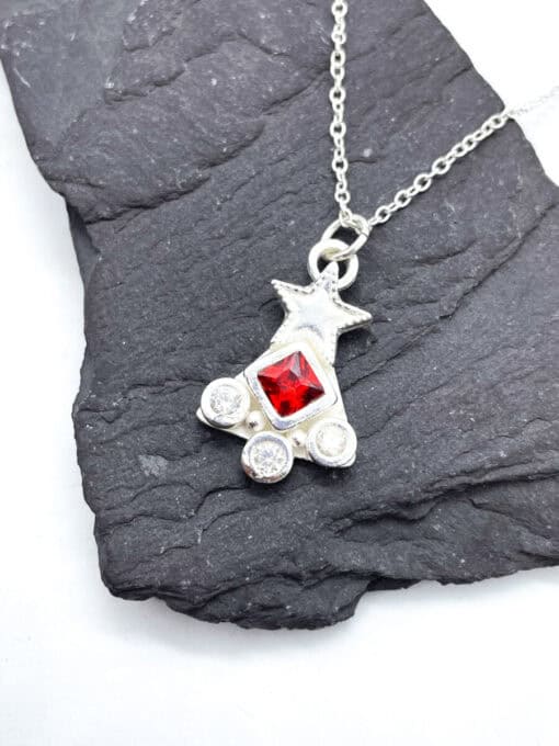 Silver necklace with a star and three gems, featuring a red central gem, displayed on a dark textured background.