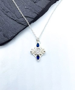 Silver necklace with blue and clear gemstone pendant lying on a dark surface.